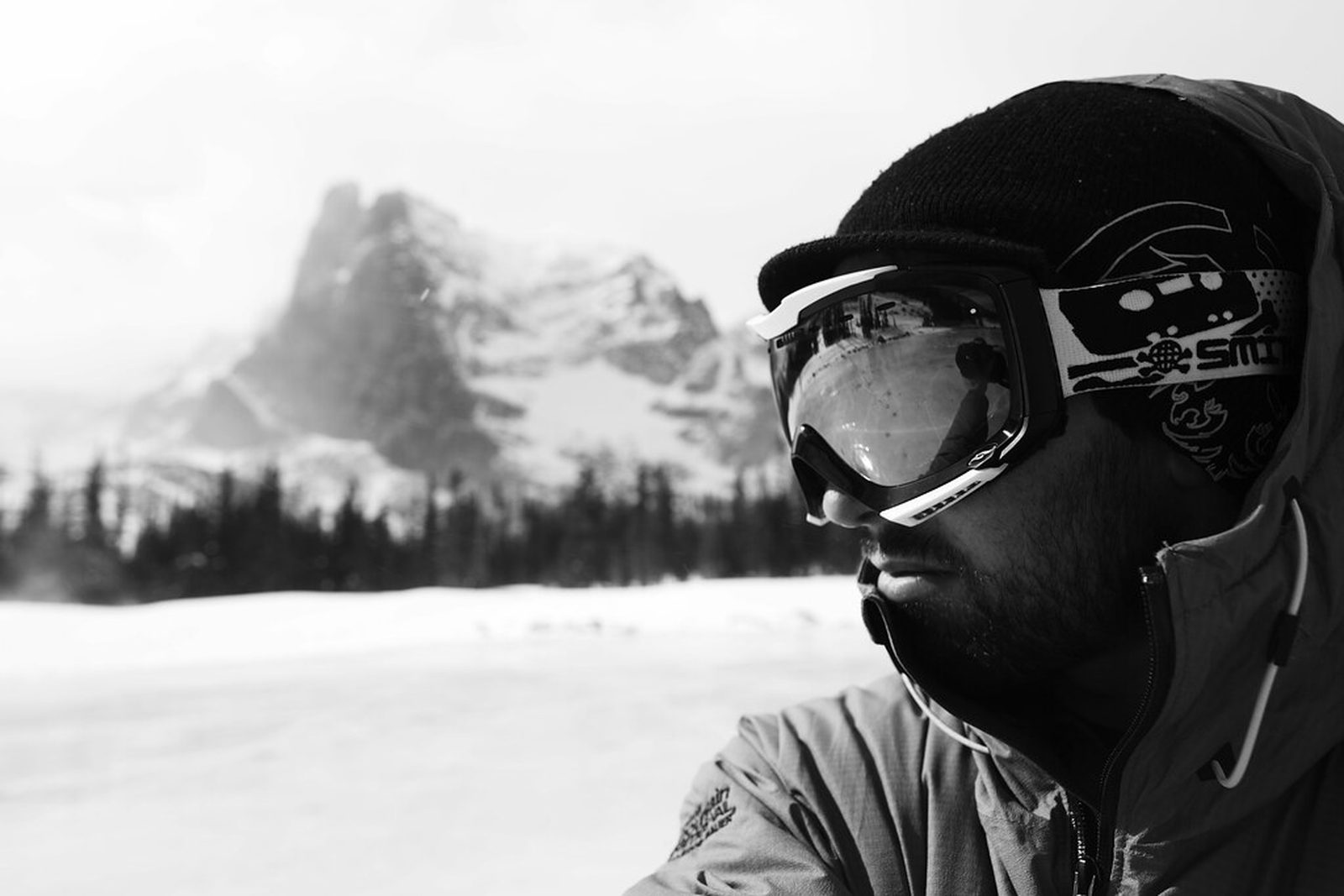 Skier in goggles and a hood in front of a snowy mountain face